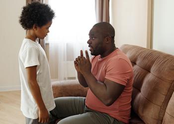 Man sitting on couch talk to his son who stands before him